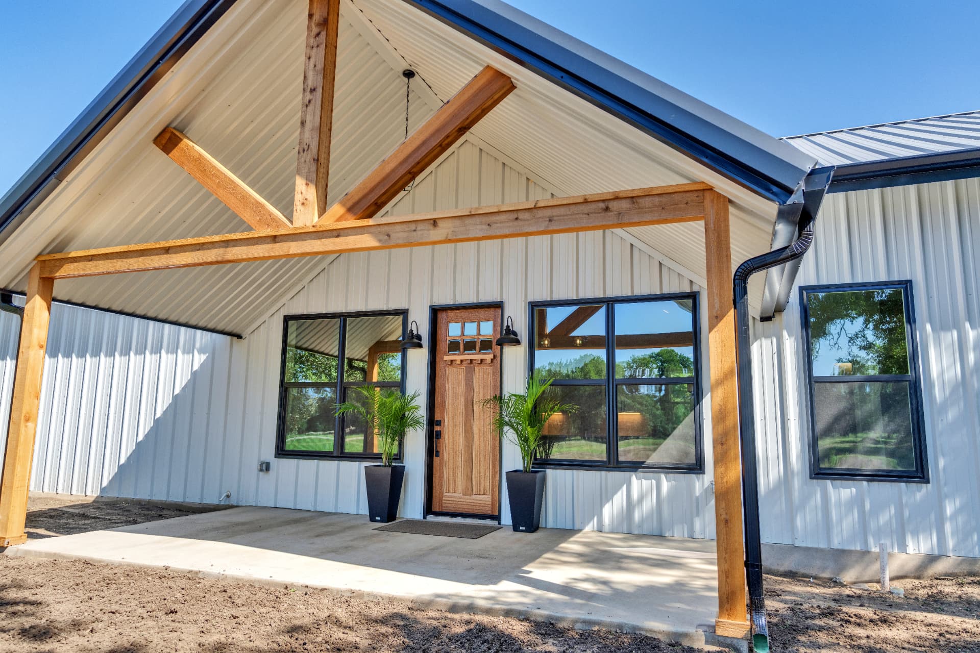 Custom barndominium entry with cedar timber porch and black steel windows in Central Texas